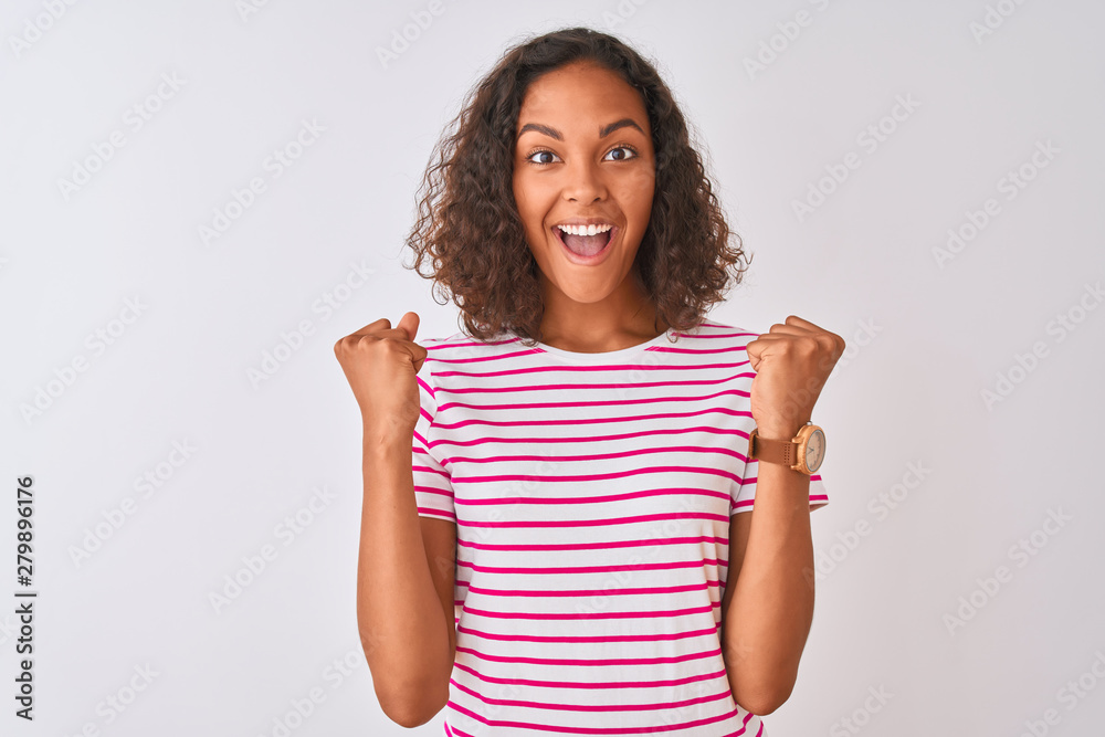 Young brazilian woman wearing pink striped t-shirt standing over isolated white background celebrating surprised and amazed for success with arms raised and open eyes. Winner concept. Young brazilian woman wearing pink striped t-shirt standing over isolated white background celebrating surprised and amazed for success with arms raised and open eyes. Winner concept.