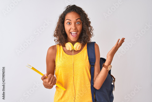 Brazilian student woman wearing backpack holding notebook over isolated white background very happy and excited, winner expression celebrating victory screaming with big smile and raised hands