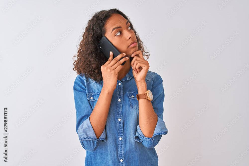 Young brazilian woman talking on the smartphone standing over isolated white background serious face thinking about question, very confused idea