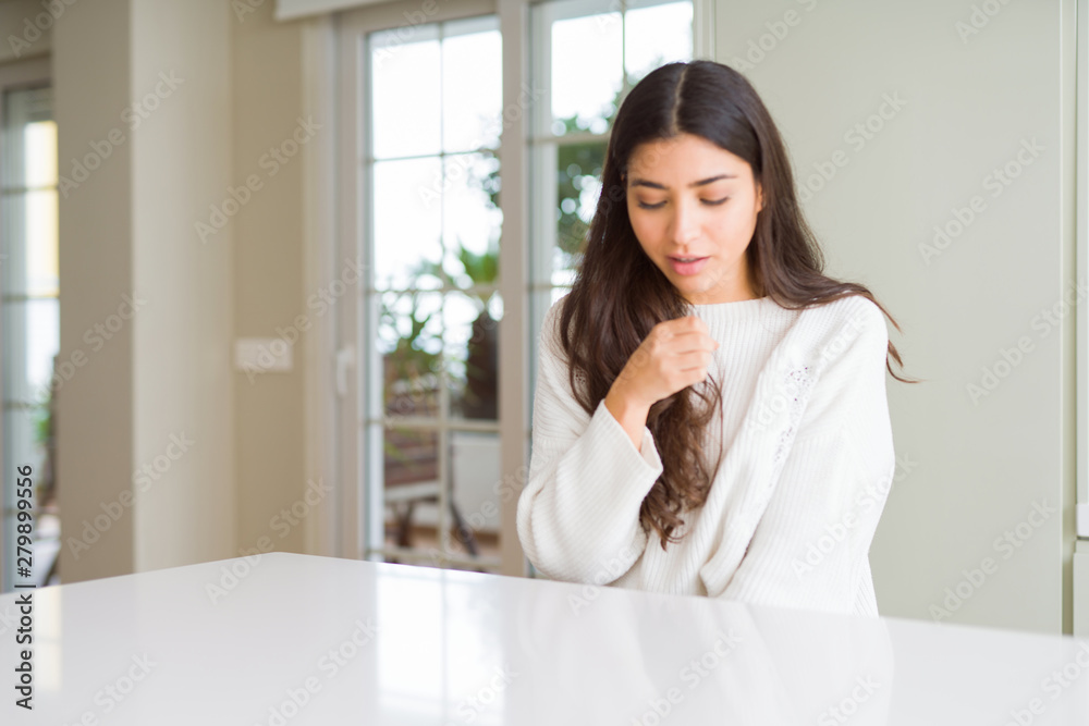 Young beautiful woman at home on white table feeling unwell and coughing as symptom for cold or bronchitis. Healthcare concept.