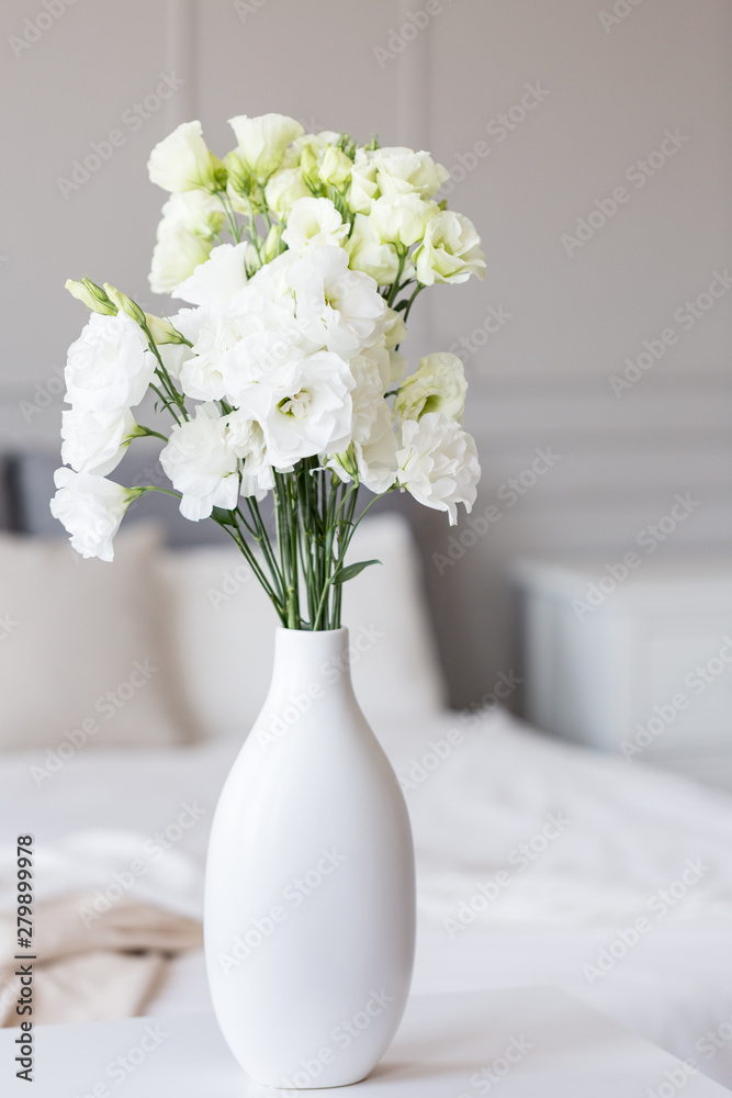 White flowers in vase in elegant grey bedroom interior with simple bedding White flowers in vase in elegant grey bedroom interior with simple bedding