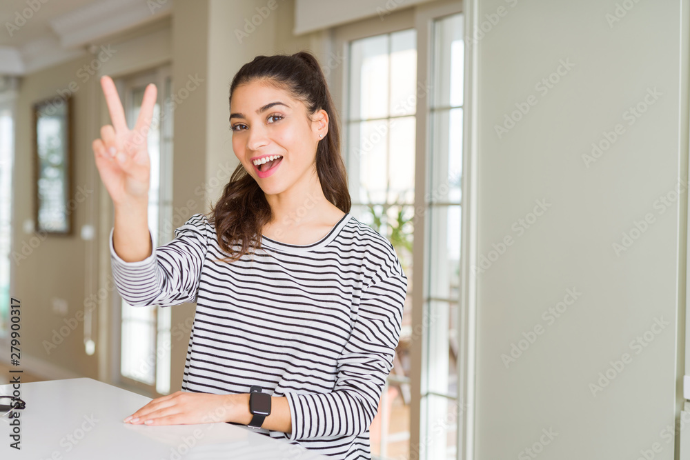 Young beautiful woman at home smiling with happy face winking at the camera doing victory sign. Number two. Young beautiful woman at home smiling with happy face winking at the camera doing victory sign. Number two.