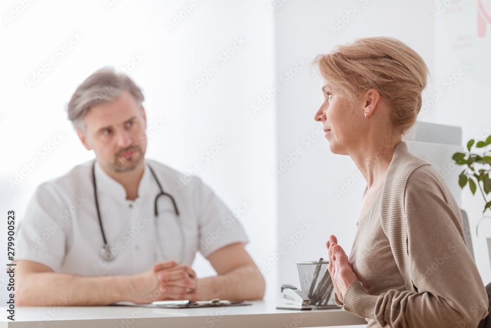 Handsome middle age doctor and female patient at hospital office Handsome middle age doctor and female patient at hospital office