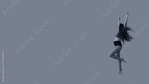 Young beautiful pregnant woman with long healthy curly hair dancing in black underwear on blue isolated background banner. Active pregnancy. Black and white image.