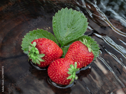 Strawberries in the water. Three berries of ripe strawberries on a green leaf. Close-up. Still life.