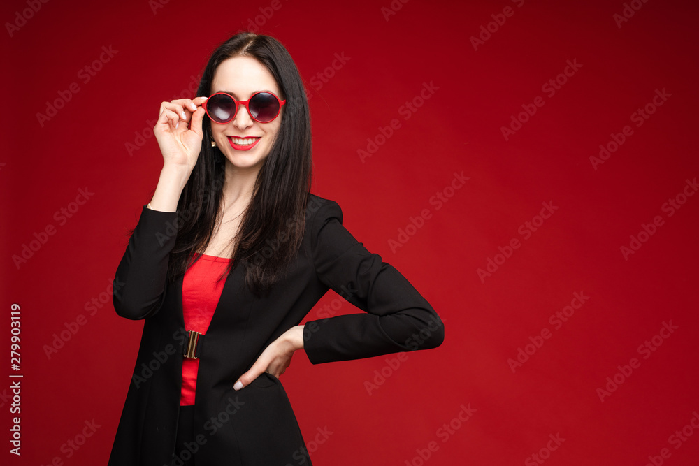 Portrait of young beautiful woman thoughtfully looking down. Brunette model in elegant costume posing at camera . Pretty lady in red sunglasses leaning one hand on other and holding it near face. Portrait of young beautiful woman thoughtfully looking down. Brunette model in elegant costume posing at camera . Pretty lady in red sunglasses leaning one hand on other and holding it near face.