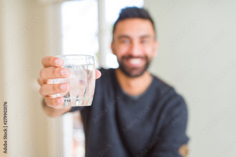Handsome hispanic man drinking a fresh glass of water with a happy face standing and smiling with a confident smile showing teeth Handsome hispanic man drinking a fresh glass of water with a happy face standing and smiling with a confident smile showing teeth