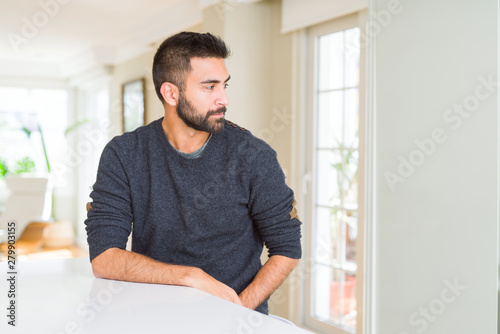 Handsome hispanic man wearing casual sweater at home looking to side, relax profile pose with natural face with confident smile.