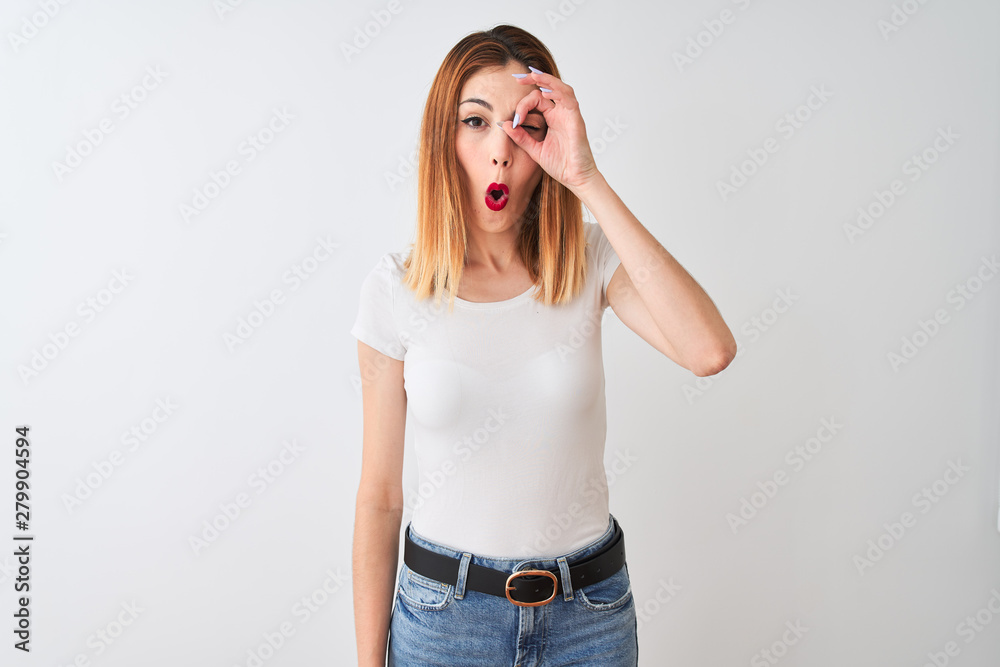 Beautiful redhead woman wearing casual t-shirt standing over isolated white background doing ok gesture shocked with surprised face, eye looking through fingers. Unbelieving expression. Beautiful redhead woman wearing casual t-shirt standing over isolated white background doing ok gesture shocked with surprised face, eye looking through fingers. Unbelieving expression.