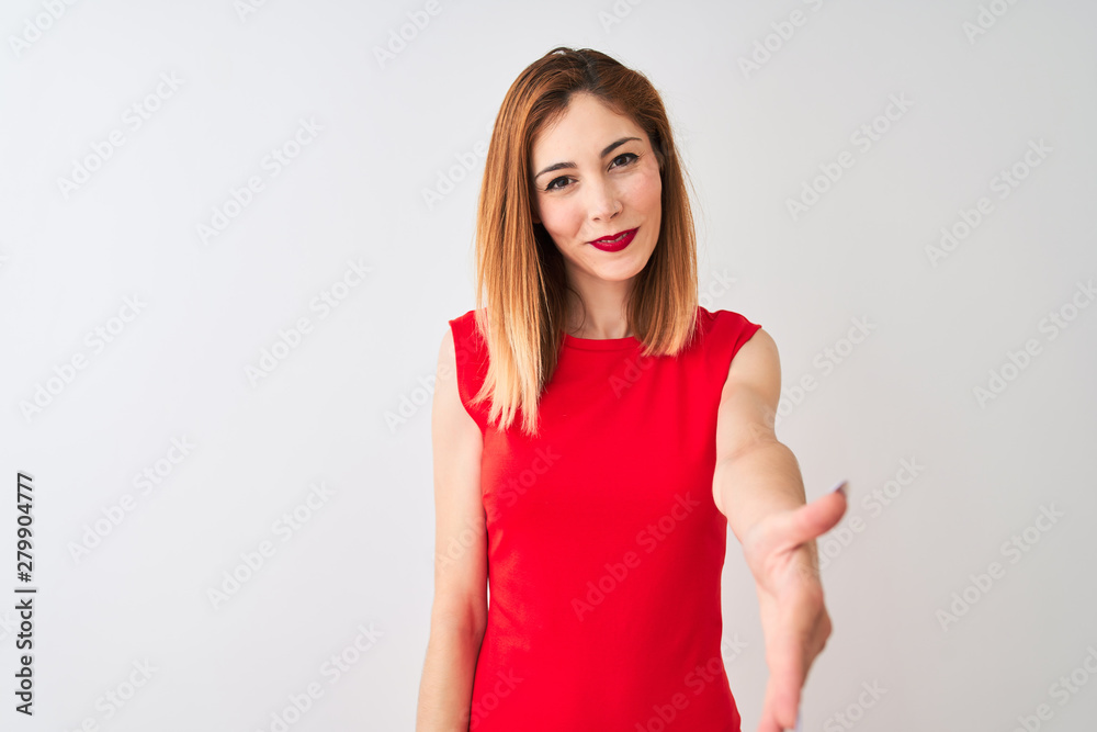 Redhead businesswoman wearing elegant red dress standing over isolated white background smiling friendly offering handshake as greeting and welcoming. Successful business. Redhead businesswoman wearing elegant red dress standing over isolated white background smiling friendly offering handshake as greeting and welcoming. Successful business.