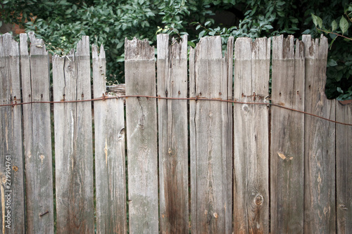 Old wooden fence with rusty bindings located in front of blurred orchard trees