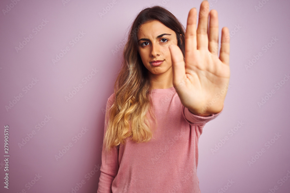 Young beautiful woman wearing a sweater over pink isolated background doing stop sing with palm of the hand. Warning expression with negative and serious gesture on the face. Young beautiful woman wearing a sweater over pink isolated background doing stop sing with palm of the hand. Warning expression with negative and serious gesture on the face.