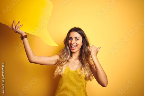 Young beautiful woman holding speech bubble over yellow isolated background pointing and showing with thumb up to the side with happy face smiling