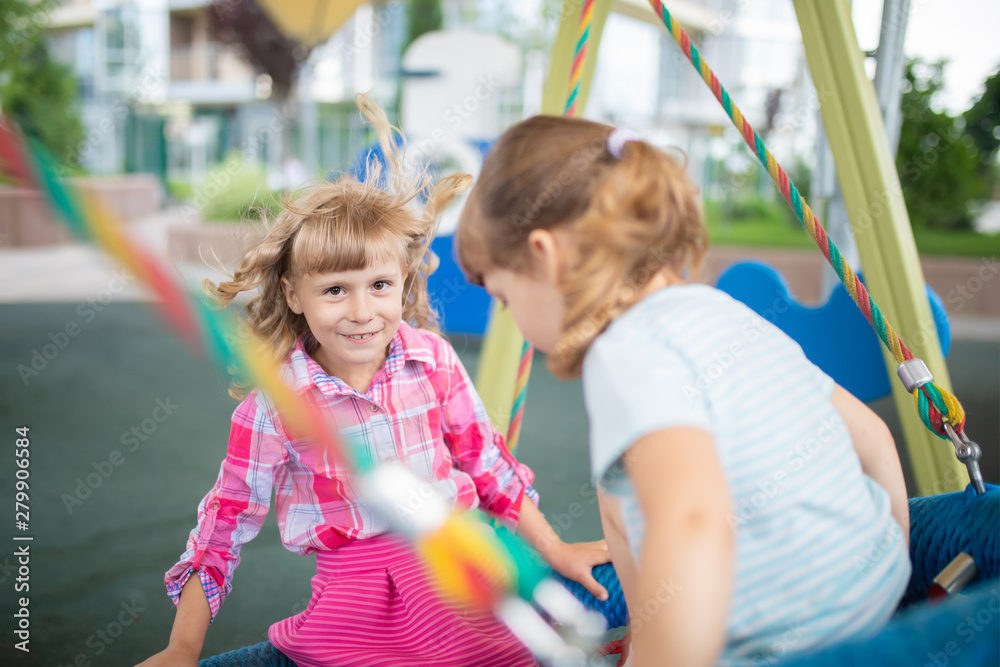 Two cute happy little girls, kids having fun on swings at playground Two cute happy little girls, kids having fun on swings at playground