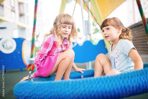 Two cute happy little girls, kids having fun on swings at playground
