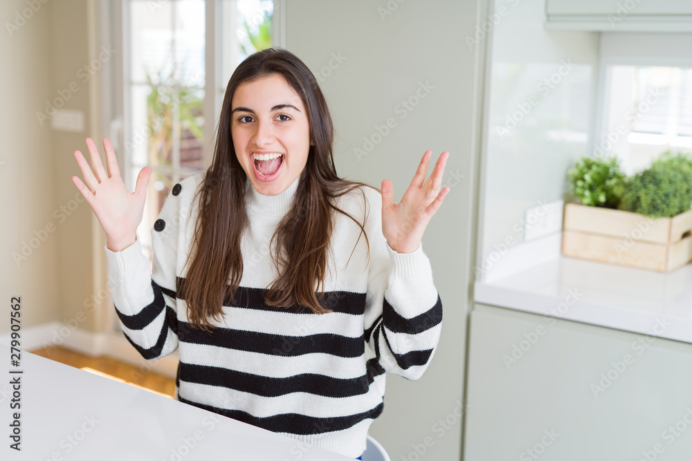 Beautiful young woman wearing stripes sweater celebrating crazy and amazed for success with arms raised and open eyes screaming excited. Winner concept Beautiful young woman wearing stripes sweater celebrating crazy and amazed for success with arms raised and open eyes screaming excited. Winner concept