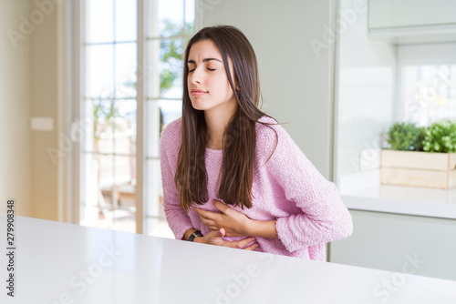 Beautiful young woman wearing pink sweater with hand on stomach because indigestion, painful illness feeling unwell. Ache concept.
