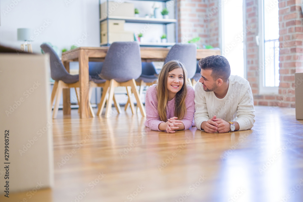 Young beautiful couple in love moving to new home, lying on the floor around cardboard boxes, very happy and cheerful for new apartment