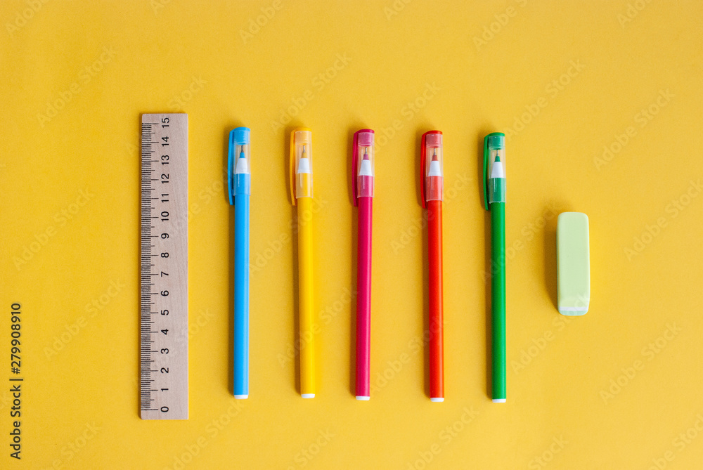 colored pens, next to a wooden ruler and an eraser, accessories for studying a yellow background colored pens, next to a wooden ruler and an eraser, accessories for studying a yellow background
