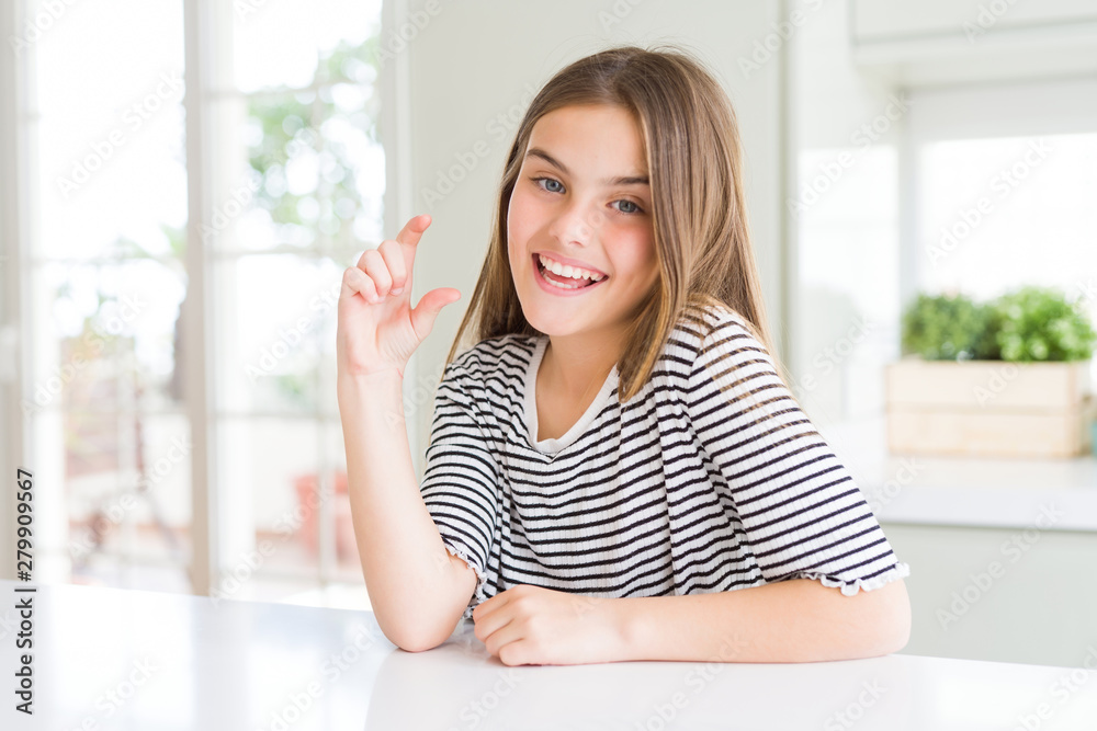 Beautiful young girl kid wearing stripes t-shirt smiling and confident gesturing with hand doing size sign with fingers while looking and the camera. Measure concept.