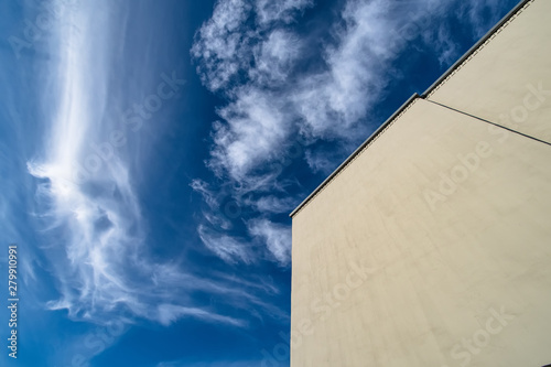 Large flat wall of a modern building without windows against a blue sky with white clouds