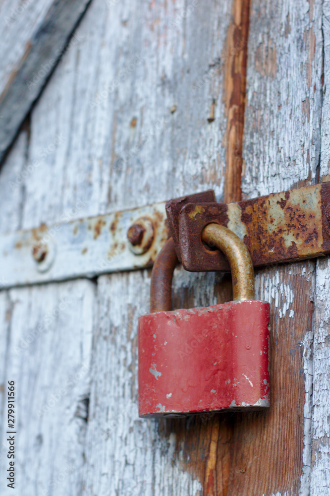Old brown padlock on a gray door with wooden planks of cracked paint and rust. Vintage gates with metal stripes and bolts