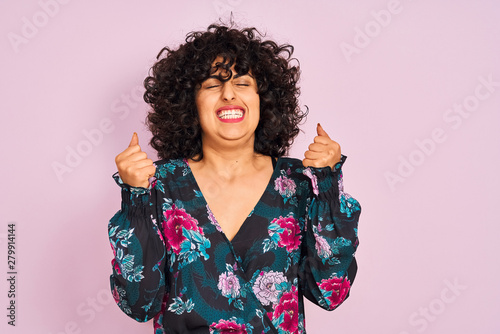 Young arab woman with curly hair wearing floral dress over isolated pink background excited for success with arms raised and eyes closed celebrating victory smiling. Winner concept.