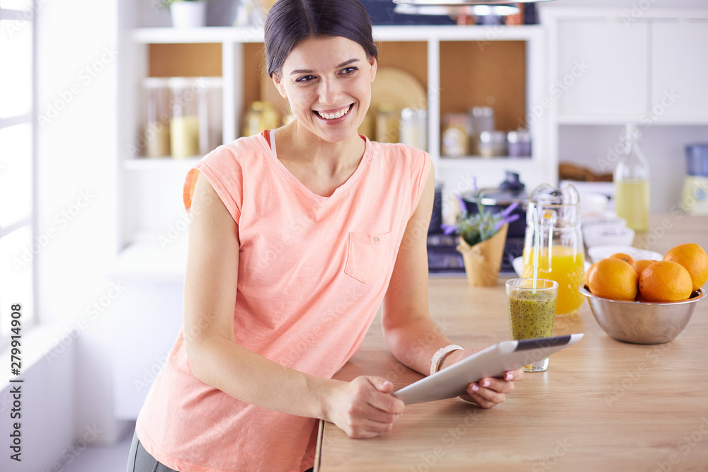 Beautiful young woman using a digital tablet in the kitchen Beautiful young woman using a digital tablet in the kitchen