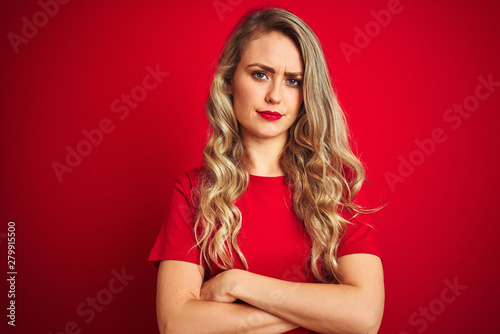 Young beautiful woman wearing basic t-shirt standing over red isolated background skeptic and nervous, disapproving expression on face with crossed arms. Negative person.