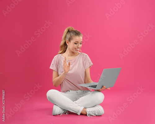 Beautiful young woman using laptop on pink background