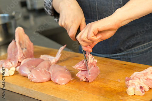 A person cuts raw chicken. Cook's hand with a knife close-up on the background of the kitchen. the woman professional chef holds raw chicken. The background is blurred