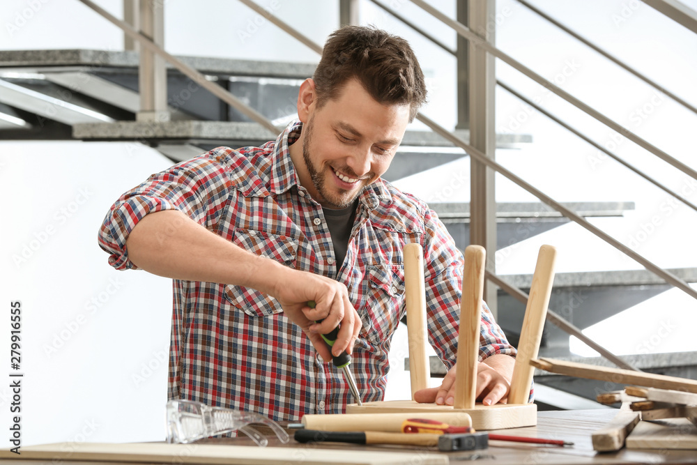 Handsome working man repairing wooden stool at table indoors Handsome working man repairing wooden stool at table indoors