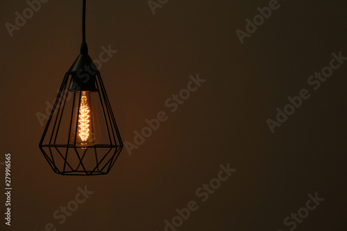 Hanging lamp bulb in chandelier against dark background, space for text