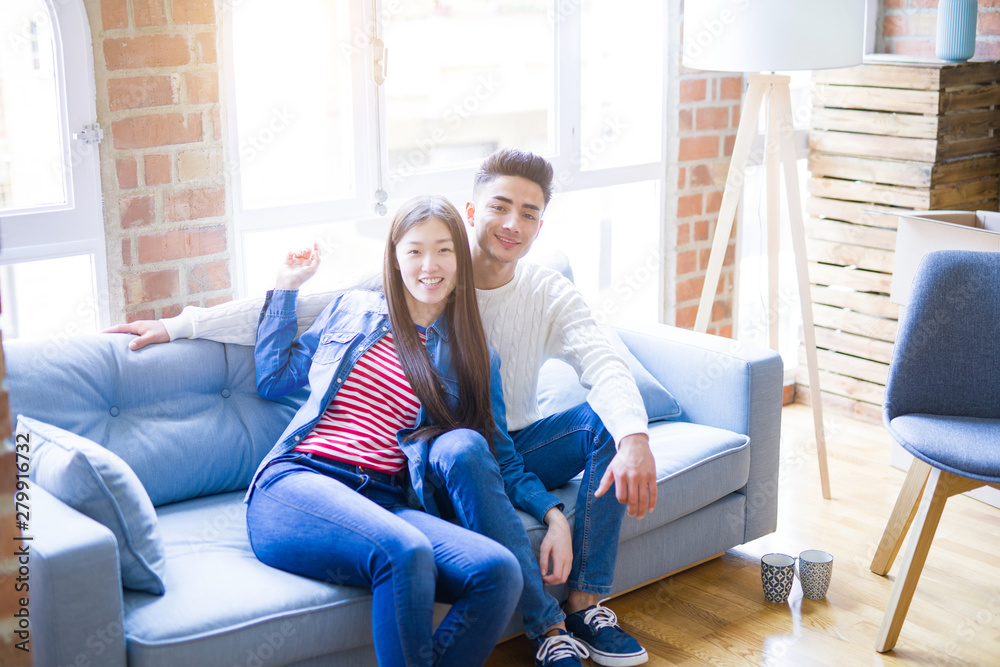 Beautiful young asian couple relaxing together sitting on the sofa arround cardboard boxes, happy moving to a new house
