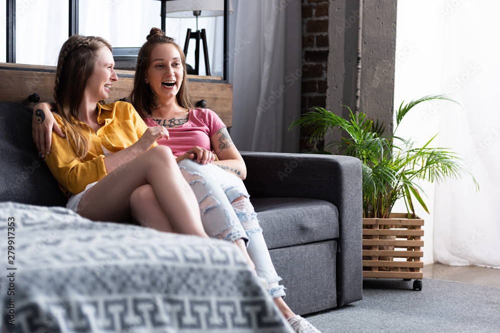 Obraz premium two pretty lesbians embracing while sitting on sofa in living room
