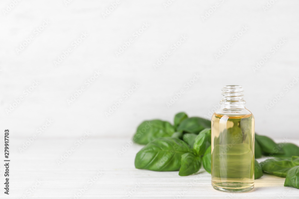 Bottle of basil essential oil on white wooden table against light background. Space for text Bottle of basil essential oil on white wooden table against light background. Space for text