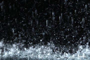 Heavy rain falling down on ground against dark background