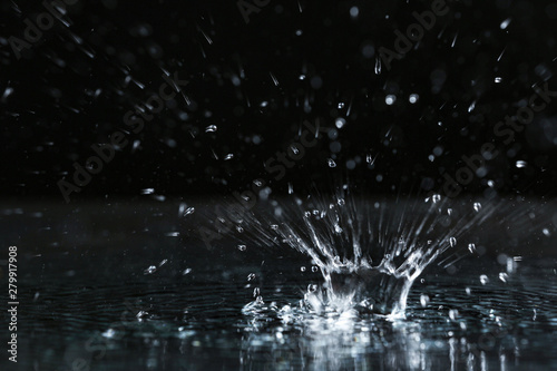Fotografie, Obraz Rain drop falling down into puddle on dark background