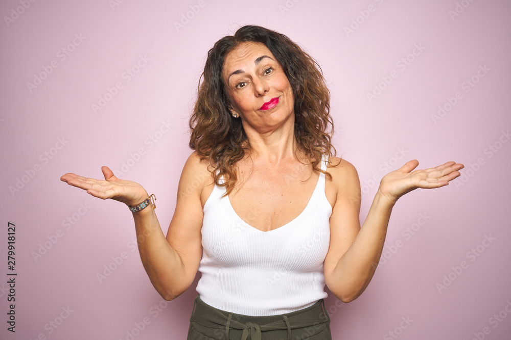 Middle age senior woman standing over pink isolated background clueless and confused expression with arms and hands raised. Doubt concept. Middle age senior woman standing over pink isolated background clueless and confused expression with arms and hands raised. Doubt concept.
