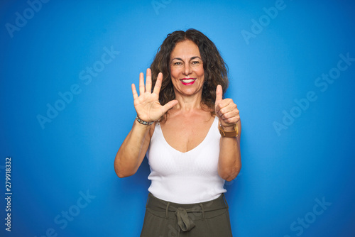 Middle age senior woman with curly hair standing over blue isolated background showing and pointing up with fingers number six while smiling confident and happy.