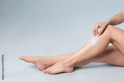 Closeup of woman touching leg with feather on grey background, space for text. Epilation procedure