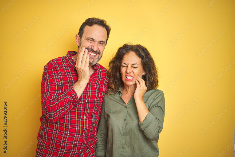 Beautiful middle age couple over isolated yellow background touching mouth with hand with painful expression because of toothache or dental illness on teeth. Dentist concept. Beautiful middle age couple over isolated yellow background touching mouth with hand with painful expression because of toothache or dental illness on teeth. Dentist concept.