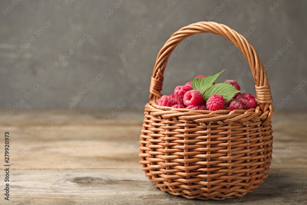 Basket of delicious fresh ripe raspberries with leaves on wooden table against grey background, space for text