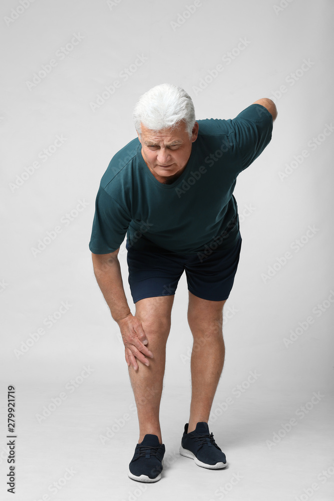 Full length portrait of senior man having knee problems on grey background Full length portrait of senior man having knee problems on grey background