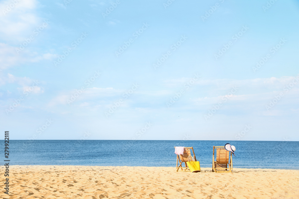 Empty wooden sunbeds and beach accessories on sandy shore