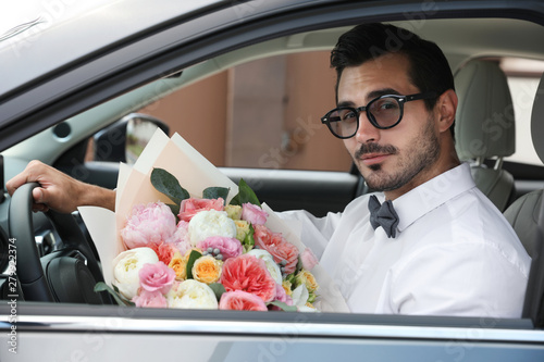Young handsome man with beautiful flower bouquet sitting in car