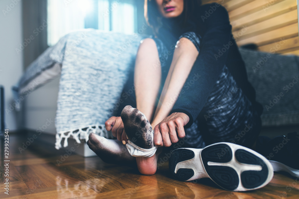 Close up of active fitness woman taking off dirty socks while sitting on  floor. Stock Photo