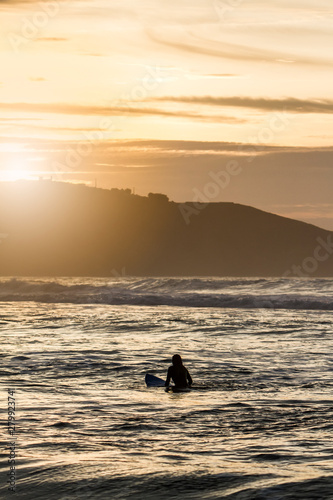 Fototapeta Naklejka Na Ścianę i Meble -  Surfer woman waiting for the perfect wave sitting on her surfboard with sunset light in northern Spain