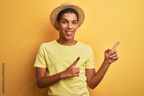 Young handsome arab man wearing t-shirt and summer hat over isolated yelllow background smiling and looking at the camera pointing with two hands and fingers to the side.