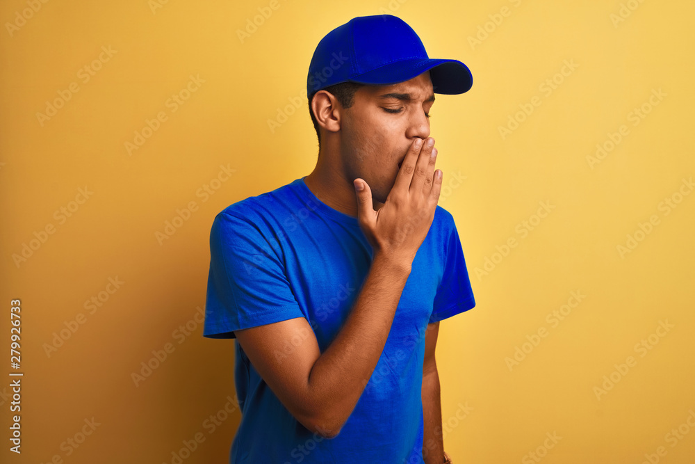 Young handsome arab delivery man standing over isolated yellow background bored yawning tired covering mouth with hand. Restless and sleepiness.